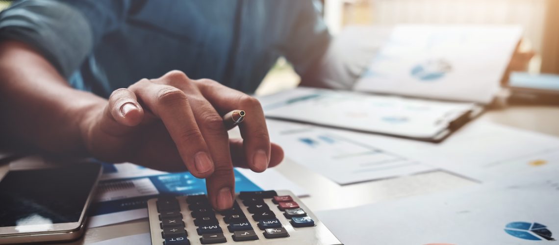 Business man using calculator with computer laptop, budget and loan paper in office